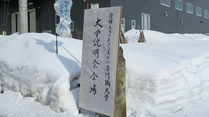 説明会の看板も雪の中。背後の黒い建物は『飯豊電池研究所』の関連施設。