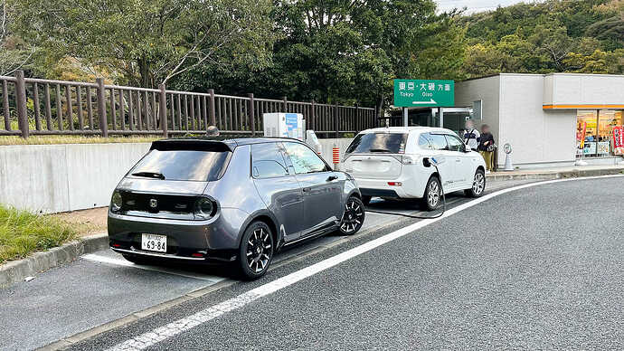 スマホアプリで前車の充電がちょうど終わりそうなタイミングなのを確認して残量21％で大磯PAにピットイン。が、アウトランダーPHEVがどうやらお替わり充電を始めたばかり。「げっ」と思いましたが、すぐにご夫婦がクルマに戻り充電器を空けてくださいました。