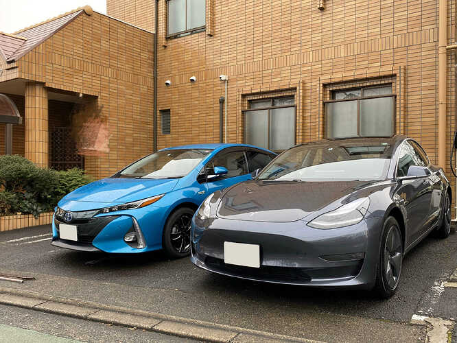 新たにやって来たBEVのテスラ・モデル3（右）と、同日に役目を終えて搬出される直前のトヨタ・プリウスPHV（左）の、短時間の出逢いの記念写真。
