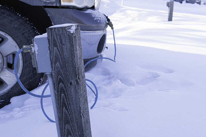 厳冬期に駐車中のエンジン凍結を防ぐ「ブロックヒーター(Vehicle Block Heater)」に電源を繋いである自動車のようす。北欧の道路沿いの「パーキングロット」には、内燃エンジンの「ウォータージャケット(水冷機構)」の凍結を防ぐヒーターへの電源供給のポールが装備されている。これに繋ぐ習慣があったお陰で、北欧では「駐めたら繋ぐ」の習慣があり、EV普及のバリアが低かったと言われている。