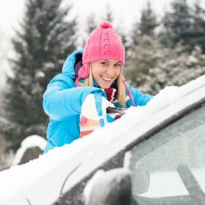 Woman cleaning car windshield of snow winter
